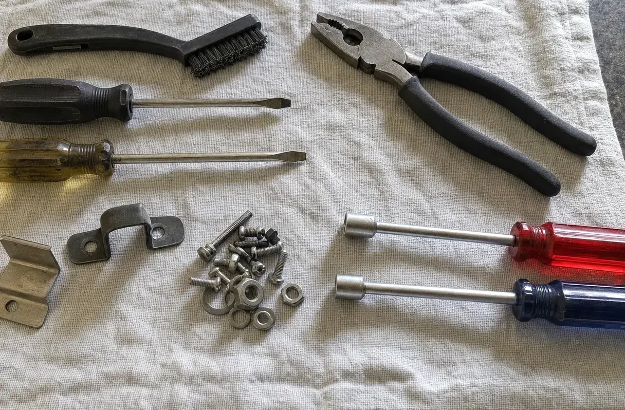 A wire brush, combination pliers, two screwdrivers and a pair of nut drivers spread across a canvas cloth