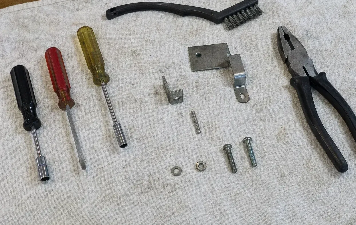 Angle brackets, bolts and washers laid on a canvas cloth beside a screwdriver, a brush and pliers