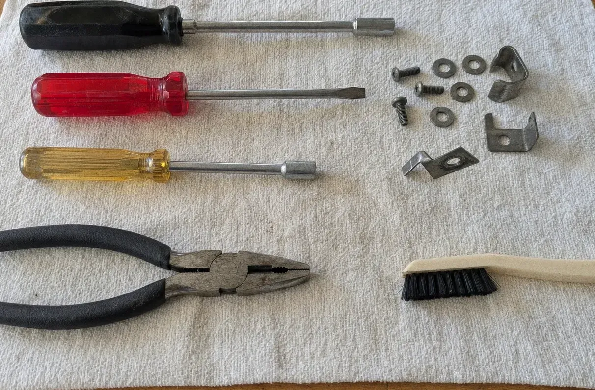 Red and yellow-handled screwdrivers, pliers and a brush on a canvas cloth with washers and flat brackets